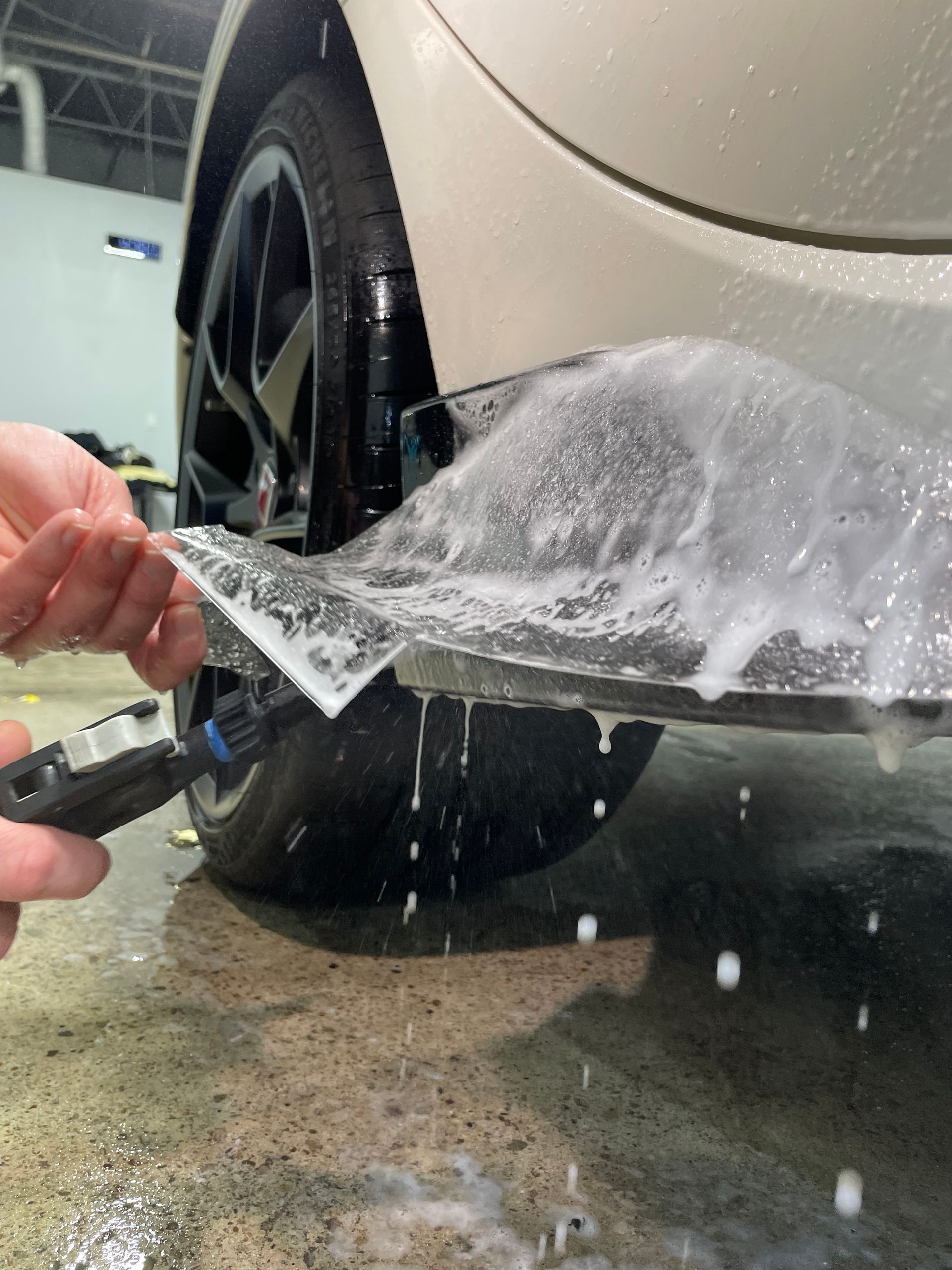 A person is using a blue squeegee to remove plastic from the hood of a car