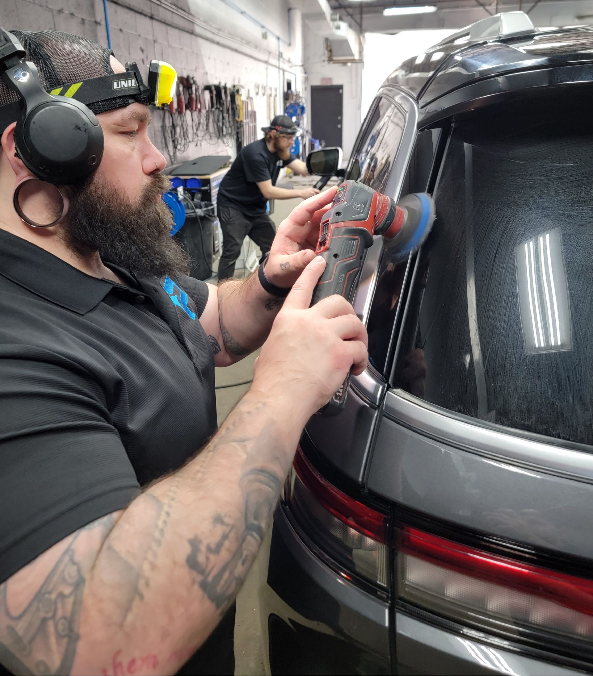 A man with a beard is polishing the back window of a car.