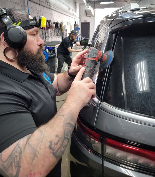 A man with a beard is polishing the back window of a car.