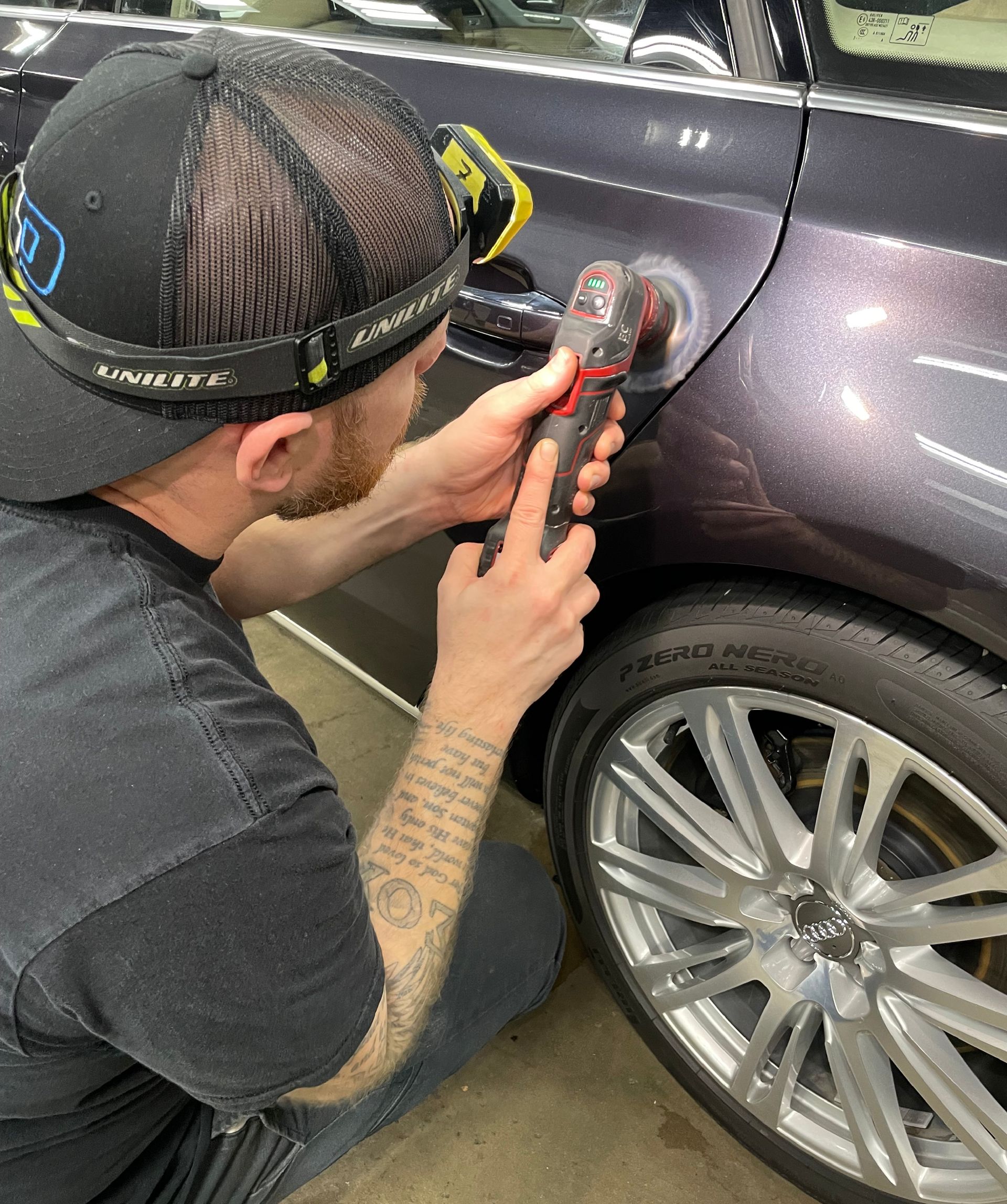 A man is cleaning the wheel of a black car with a sponge.