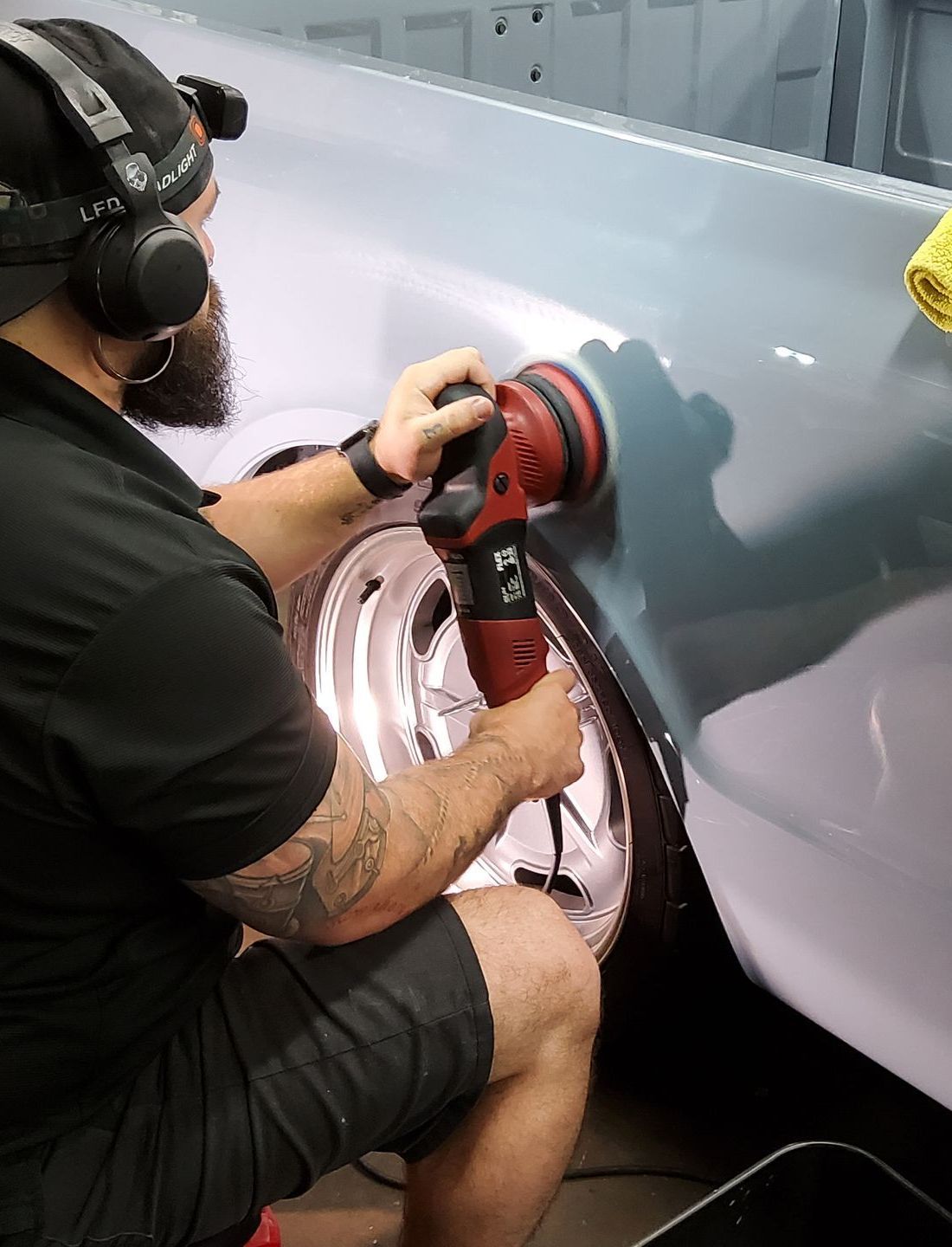 A person is using a blue squeegee to remove plastic from the hood of a car