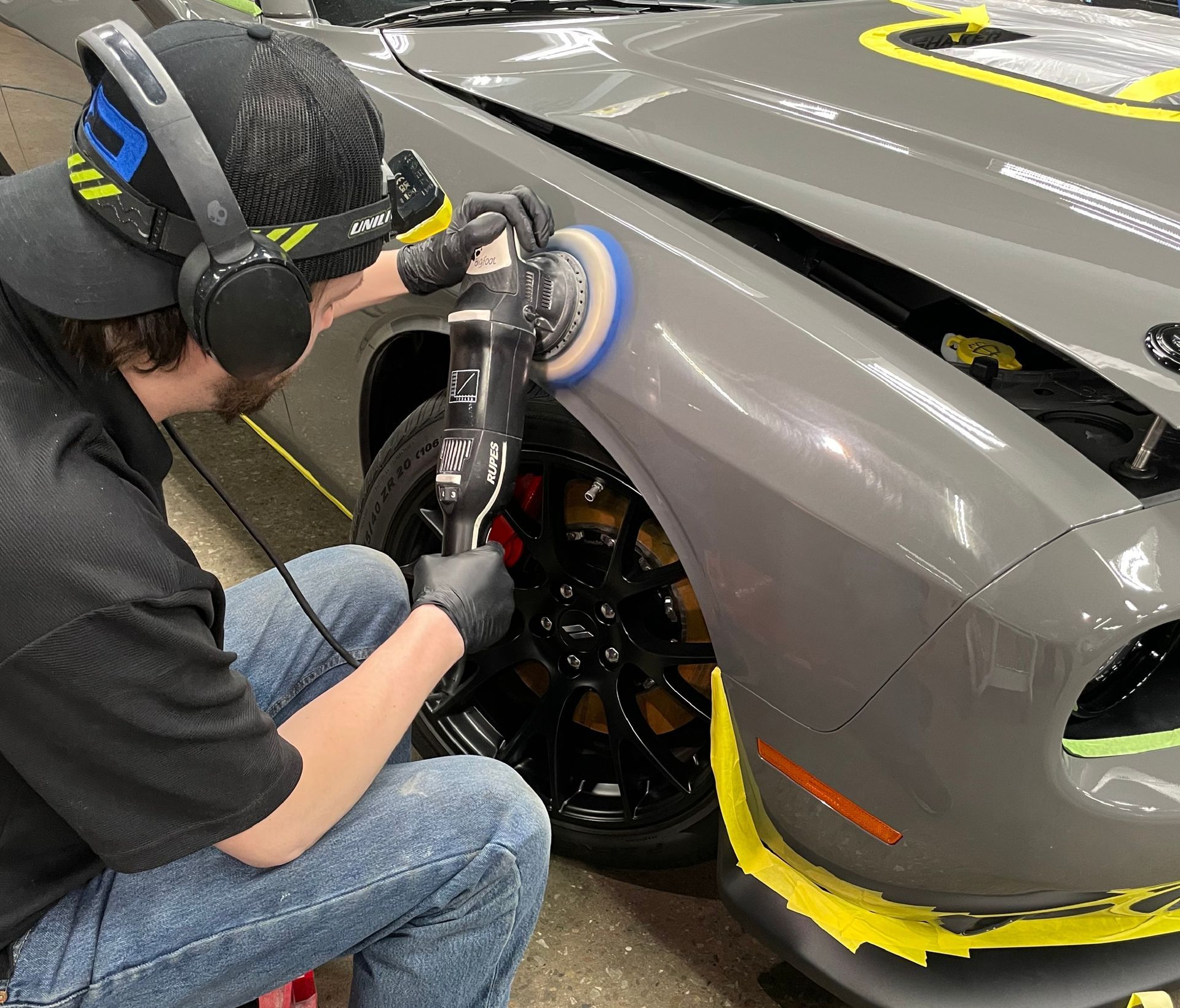A man is polishing the fender of a gray car.
