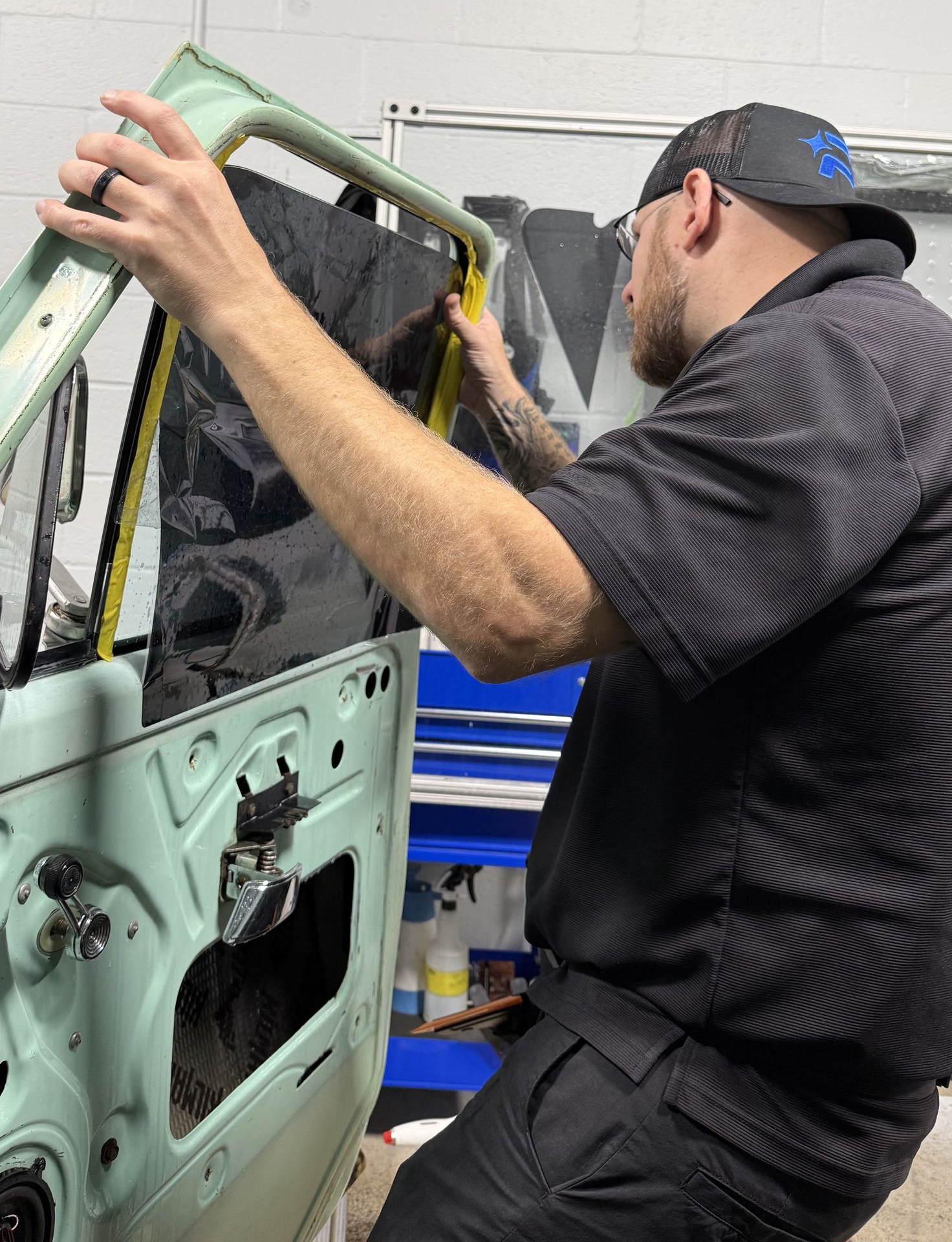 A person is using a blue squeegee to remove plastic from the hood of a car