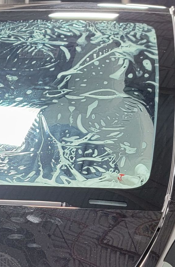 A man is cleaning the wheel of a black car with a sponge.