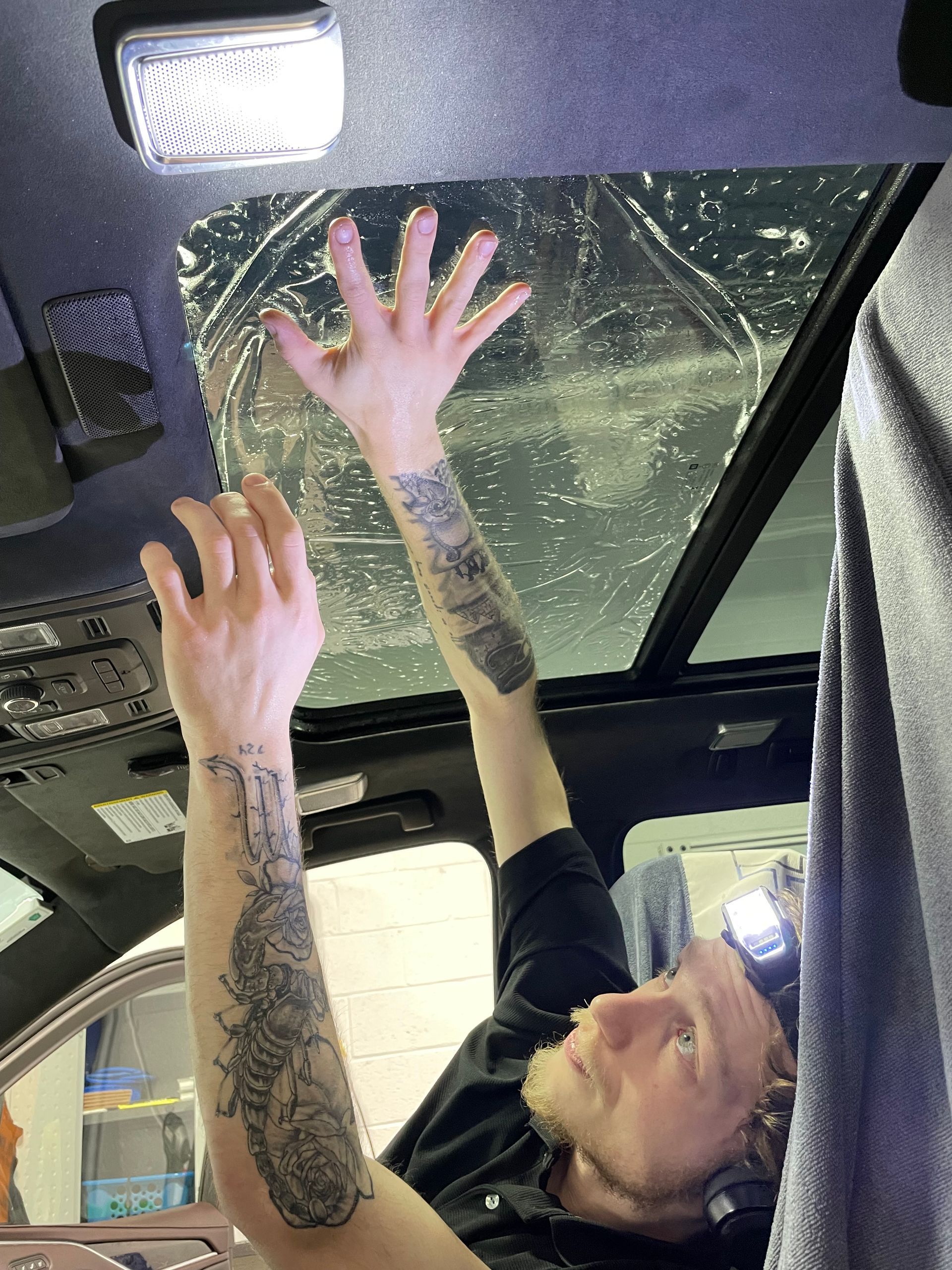 A man with a tattoo on his arm is working on the roof of a car.