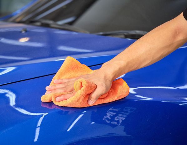 A person is cleaning a blue car with an orange towel