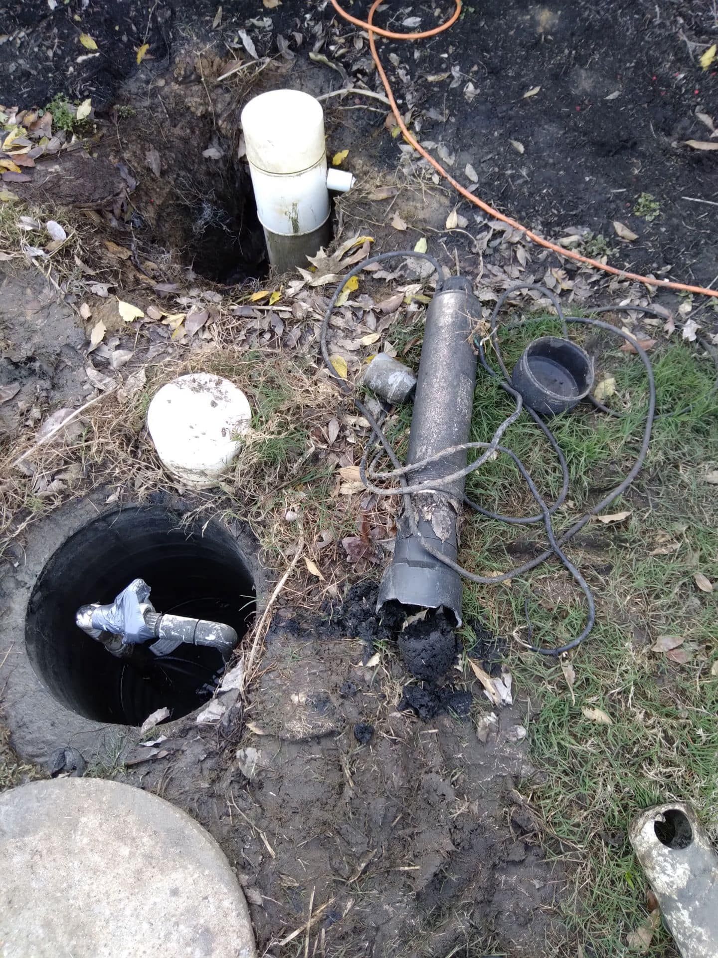 Septic system repair: open tank, damaged pipe, and excavated ground.