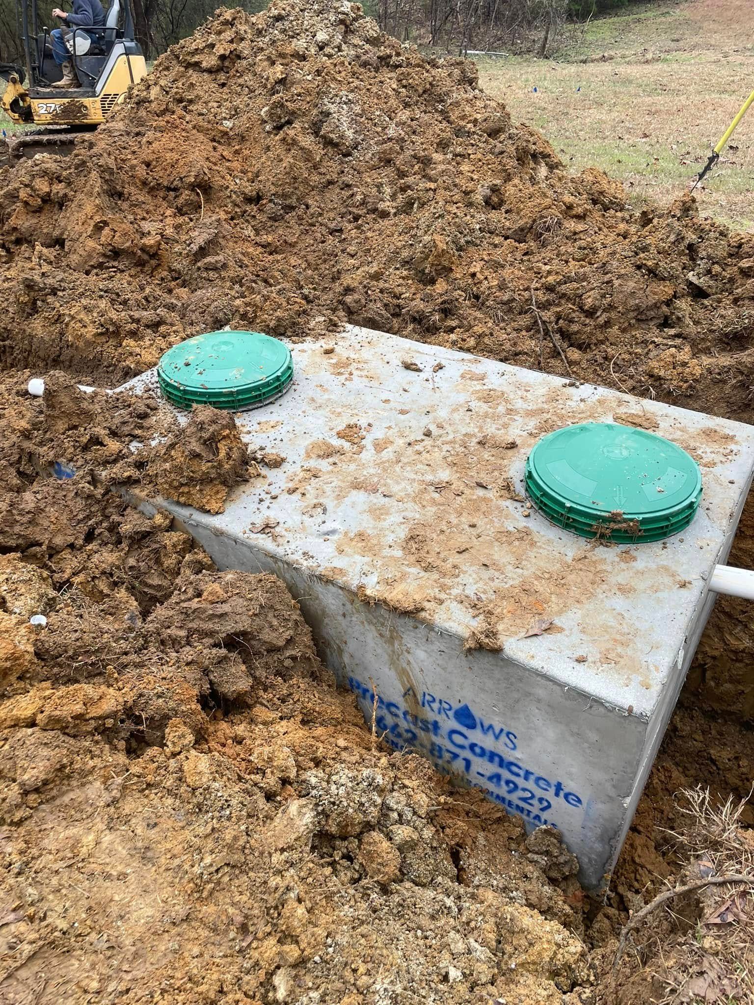 Concrete septic tank partially buried in dirt, with two green access covers.