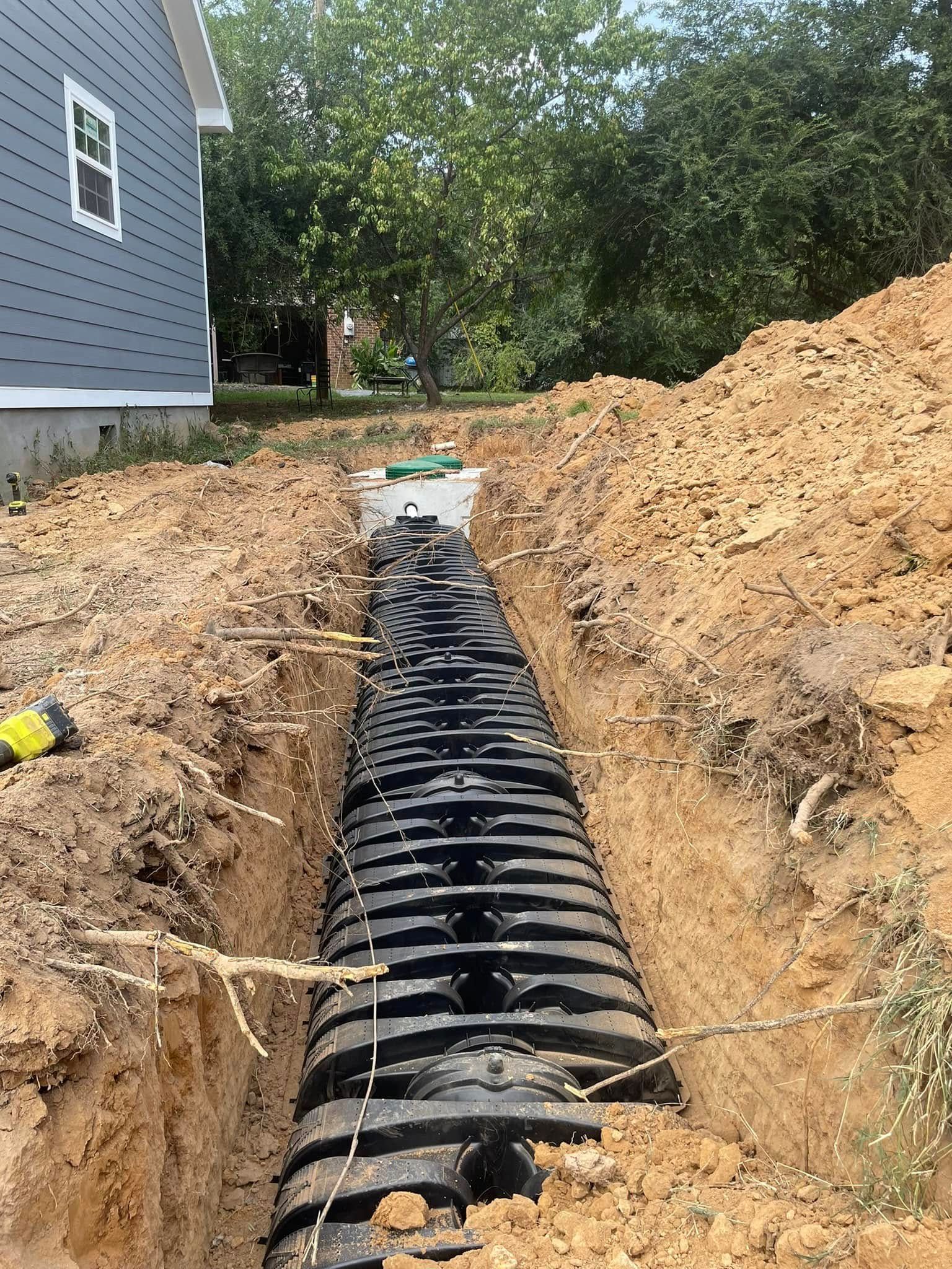 A black corrugated drain pipe in a trench, next to a house under construction.
