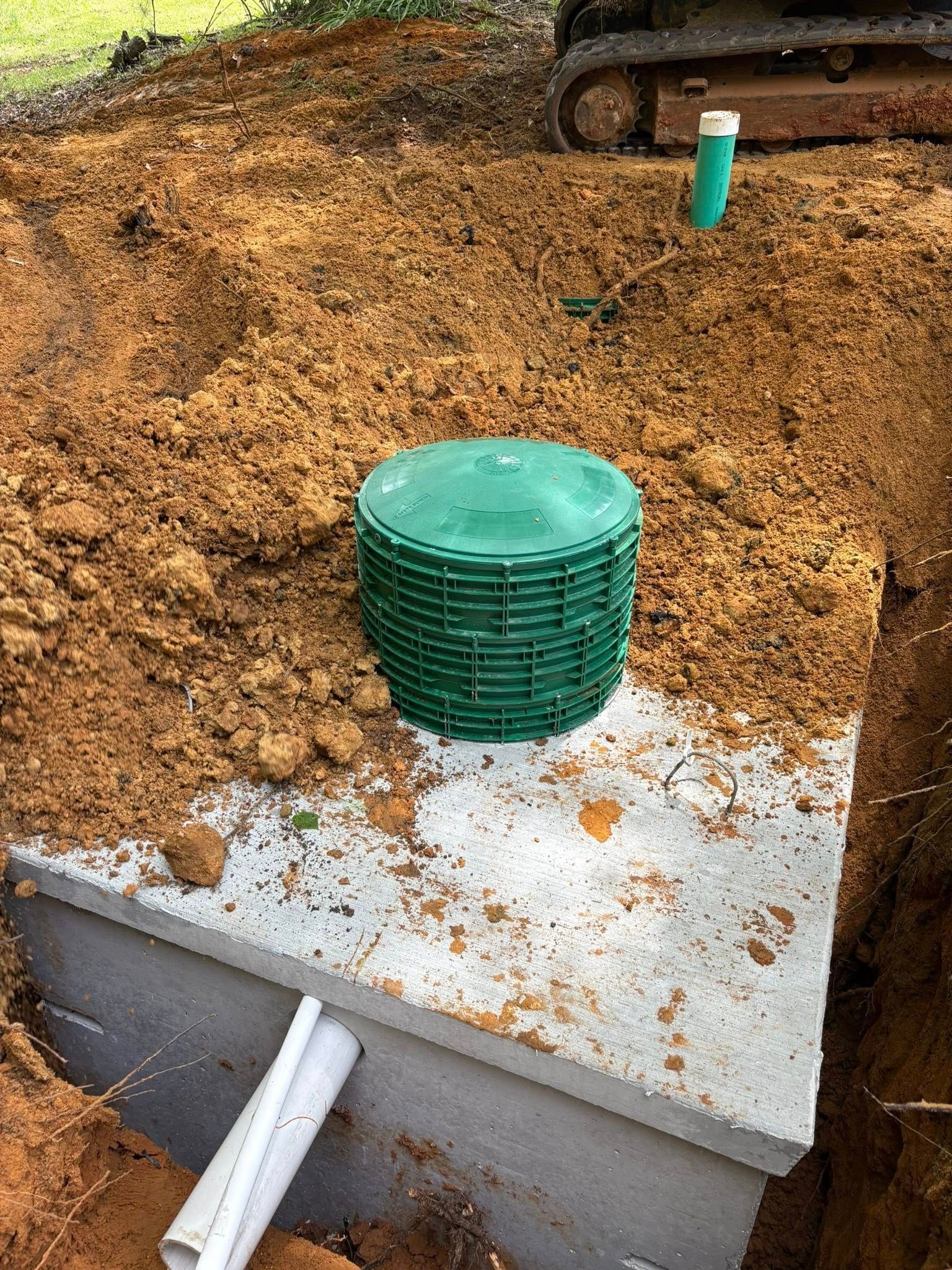 Septic system installation; green lid, concrete tank, backhoe, dirt.