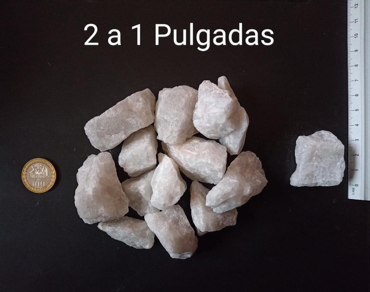 Montón de piedras blancas, de tamaño 2 a 1 pulgada, con una moneda y una regla para comparar el tamaño sobre una superficie negra.