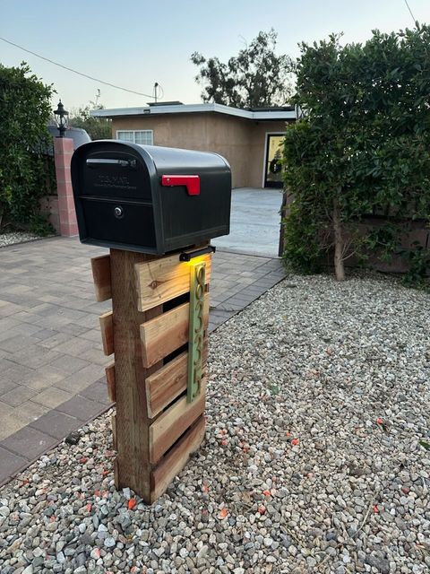 Person using a red blower in a sunny backyard, with a lattice fence and brick patio in front.