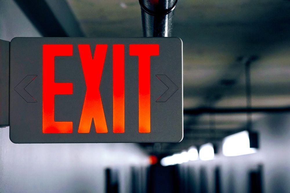 a red exit sign is hanging from the ceiling in a dark room.