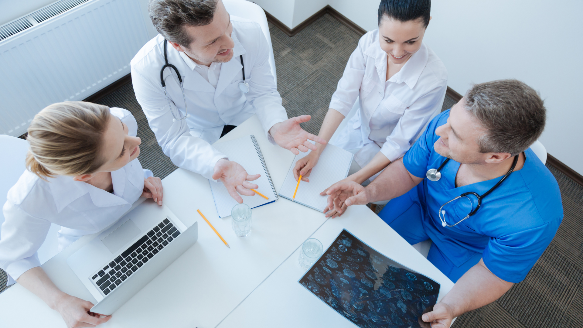 Medical team in white and blue scrubs reviewing X-rays and notes around a table