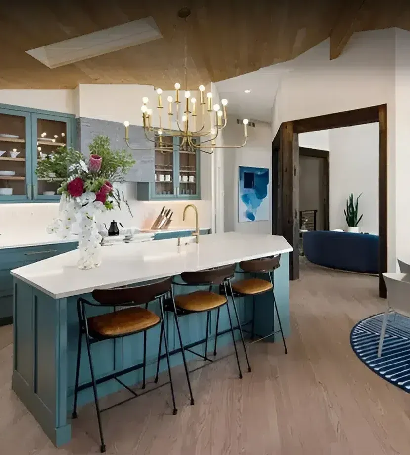 Kitchen with teal cabinets, white countertop island, gold chandelier, and wooden beams.