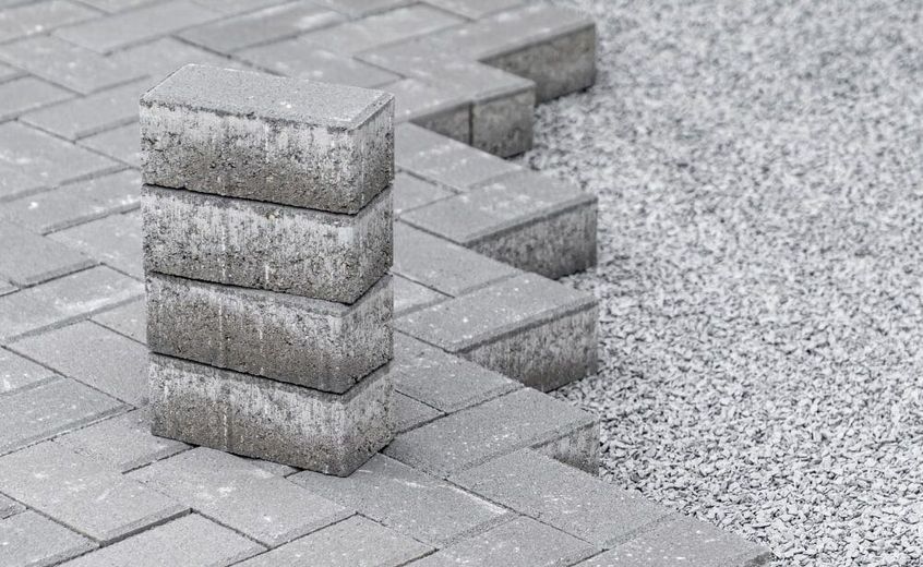 Stack of gray paving stones next to a partially laid patio with gravel base.