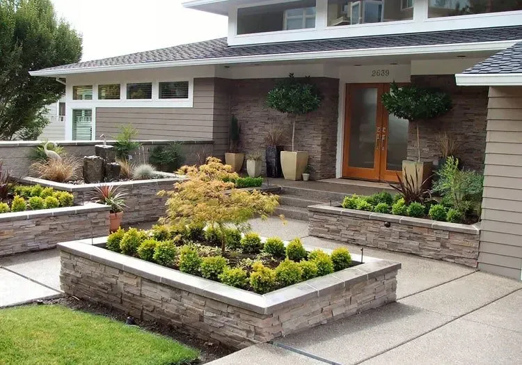 Front yard landscaping with stone planters and various plants.