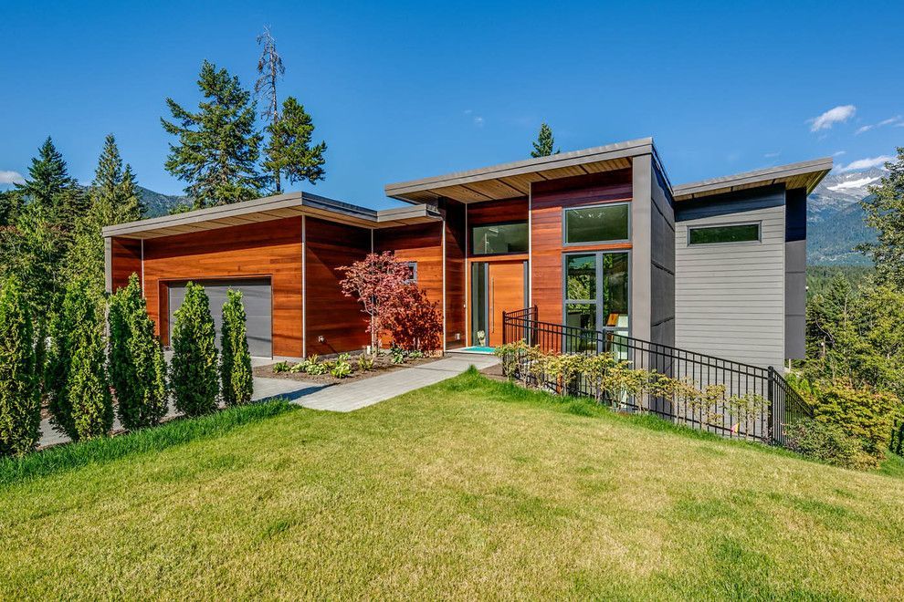 Modern home with brown wood siding, gray accents, and a sloping roof on a grassy hill, under a blue sky.