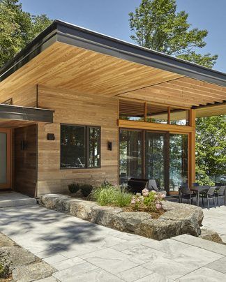 Modern lakeside home exterior with wooden siding, large windows, and a stone patio.