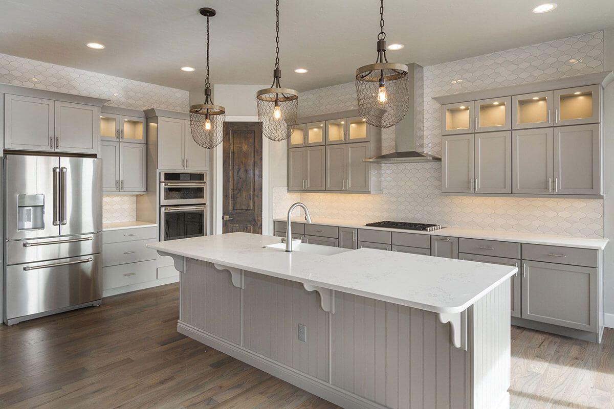 Spacious kitchen with gray cabinets, large island, stainless steel appliances, and pendant lights.
