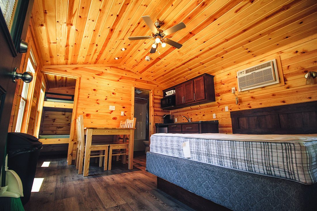 Cozy cabin interior with wood paneling. Includes a bed, table, bunk beds, and a kitchenette.