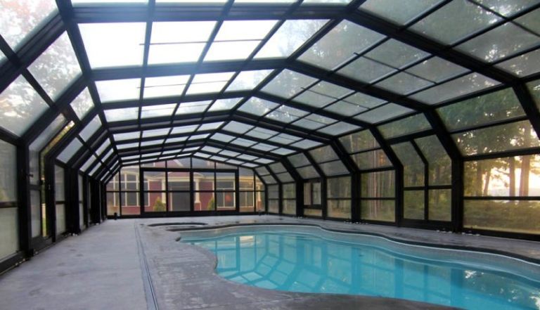 Indoor swimming pool under a black framed glass enclosure.