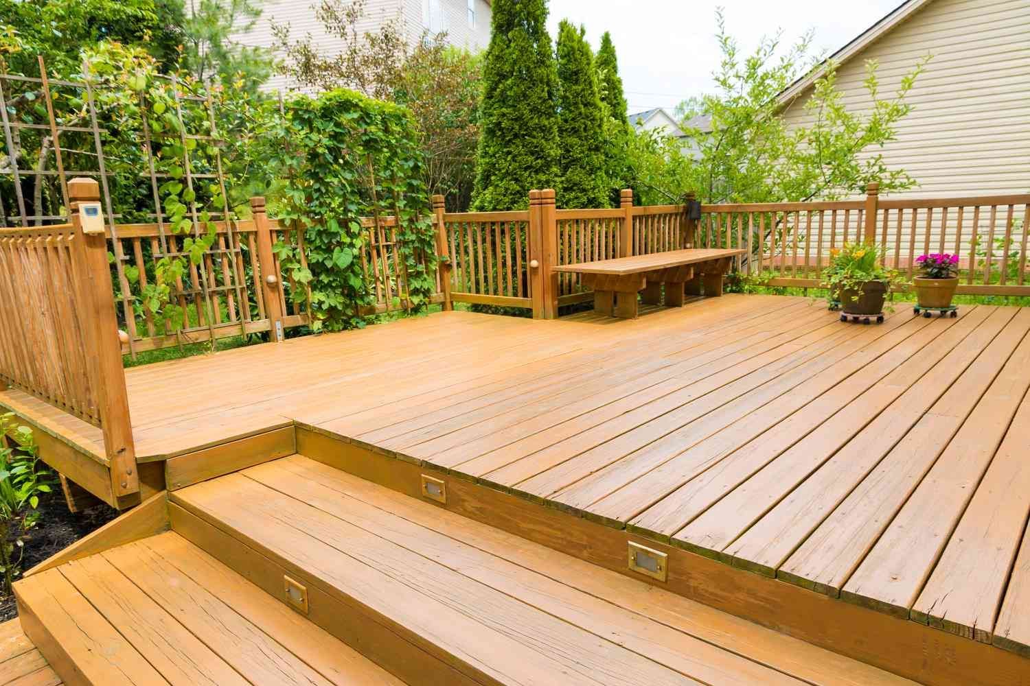 Wooden deck with steps, railing, bench, and plants in a backyard setting.