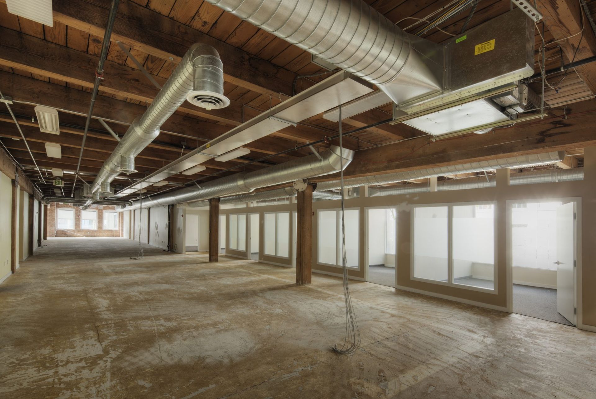 Empty interior with exposed ceiling beams, HVAC ducts, glass doors, and concrete floor.
