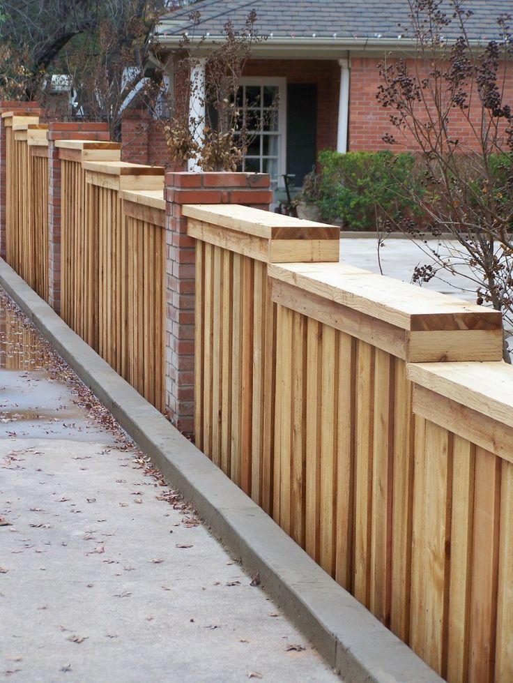 Wooden fence with brick columns bordering a concrete sidewalk, in front of a brick house.