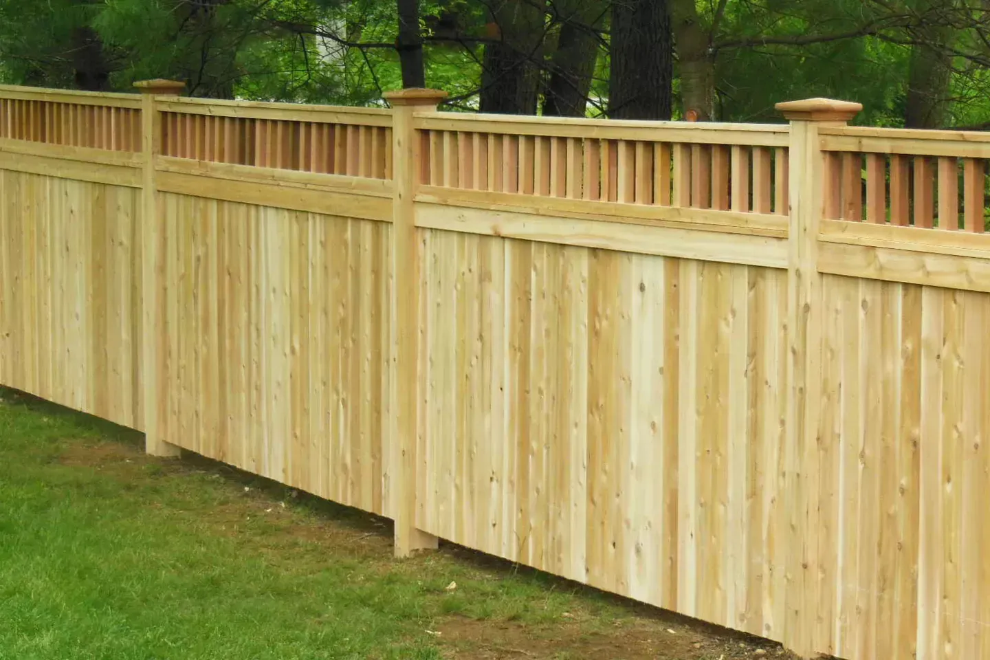 Wooden fence in a grassy yard, with a decorative top rail and posts.