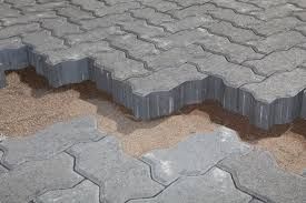 Interlocking gray concrete pavers partially laid over sand base.