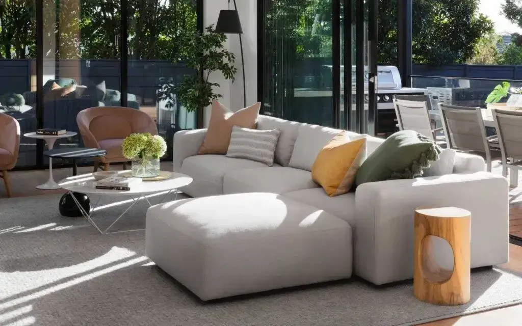 Modern living room with light gray sectional sofa, ottoman, and large windows.