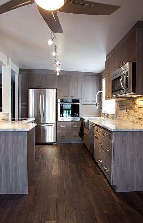 Modern kitchen with wood floors, stainless steel appliances, and gray cabinets.