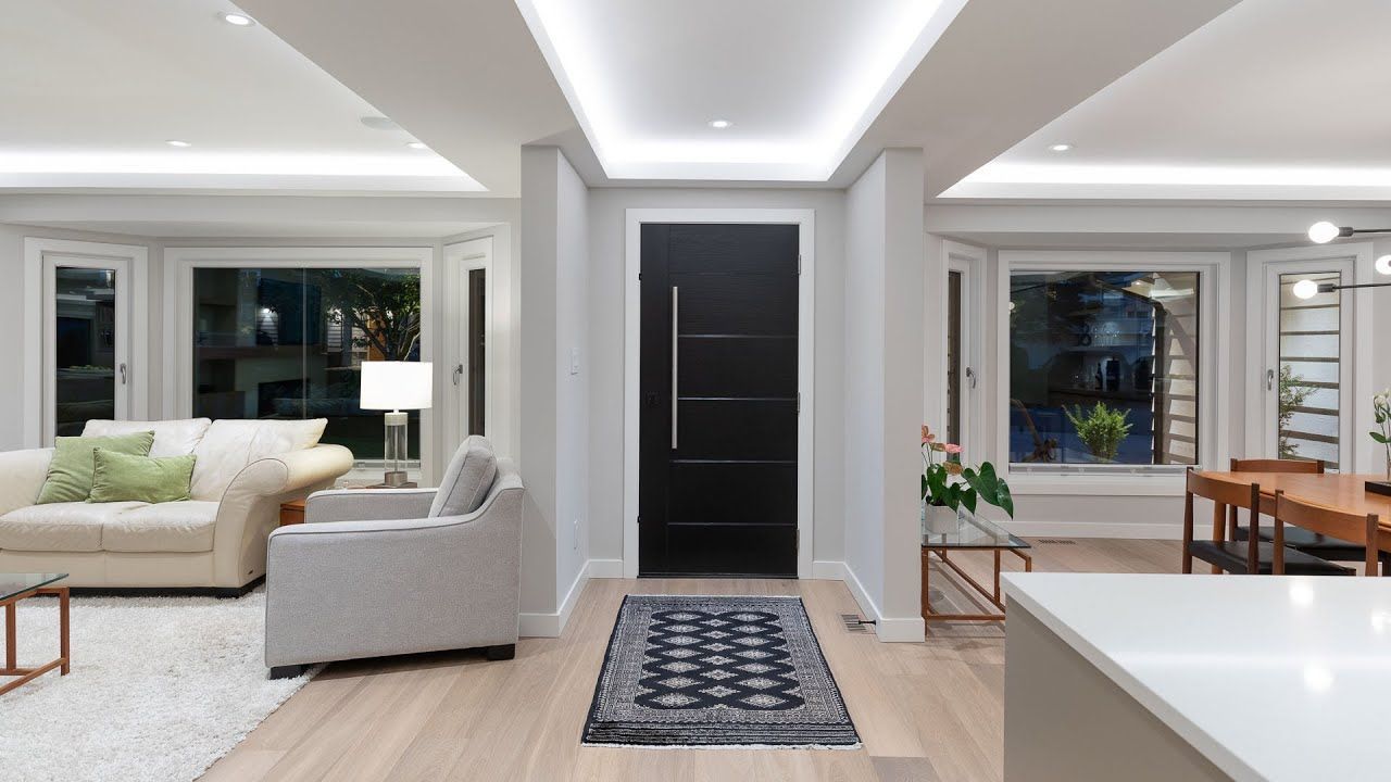 Interior view of home with black door, rug, wood floor, and large windows.