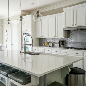 White kitchen with large island, pendant lights, and stainless steel appliances.