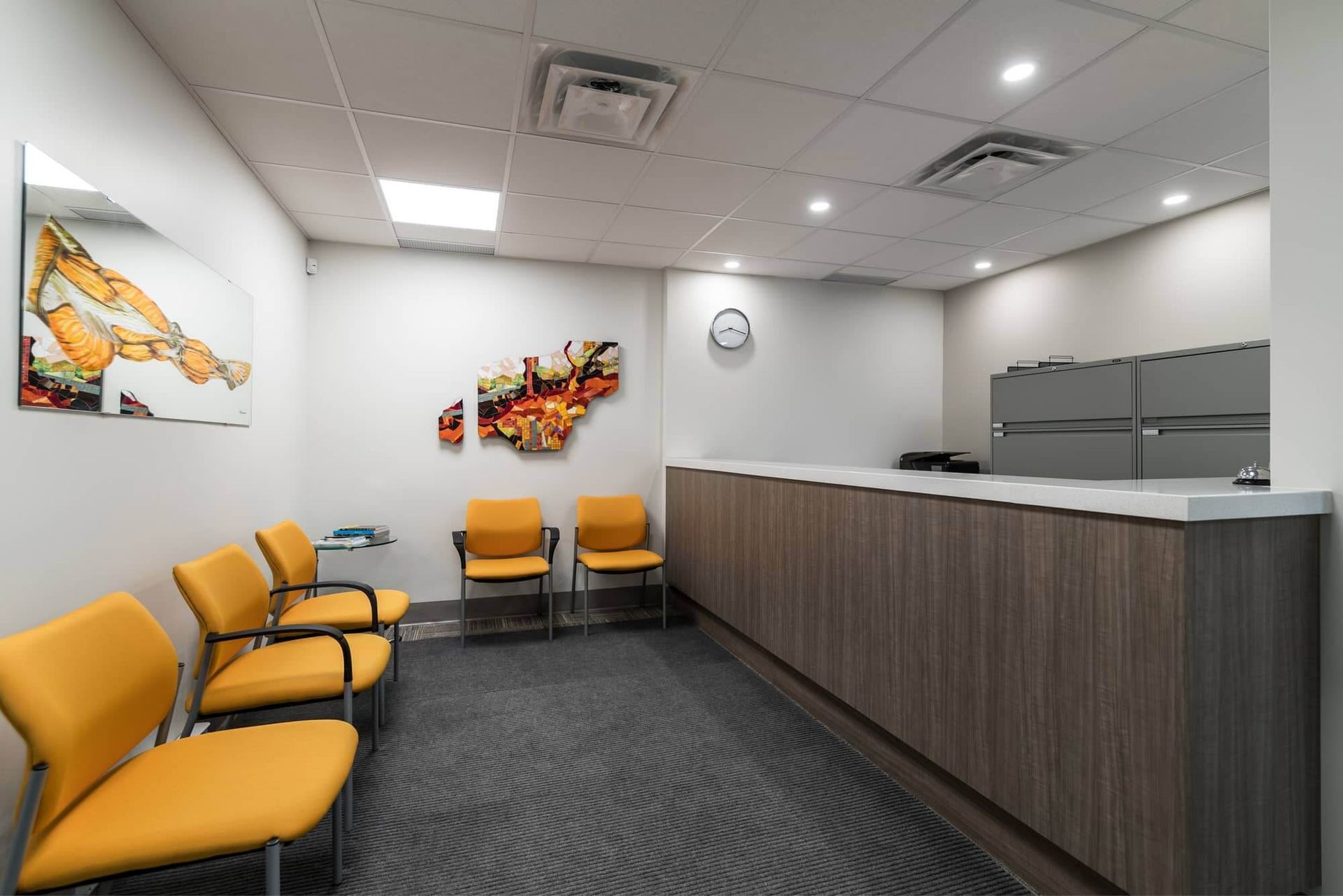 Waiting room with yellow chairs, artwork, and a reception desk.