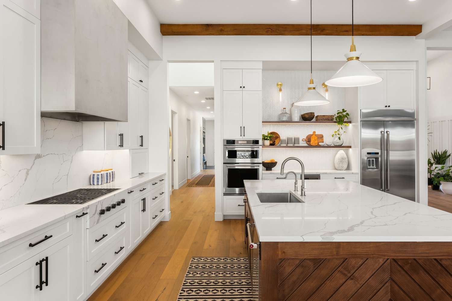 Modern white kitchen with a wooden island, marble countertops, and stainless steel appliances.