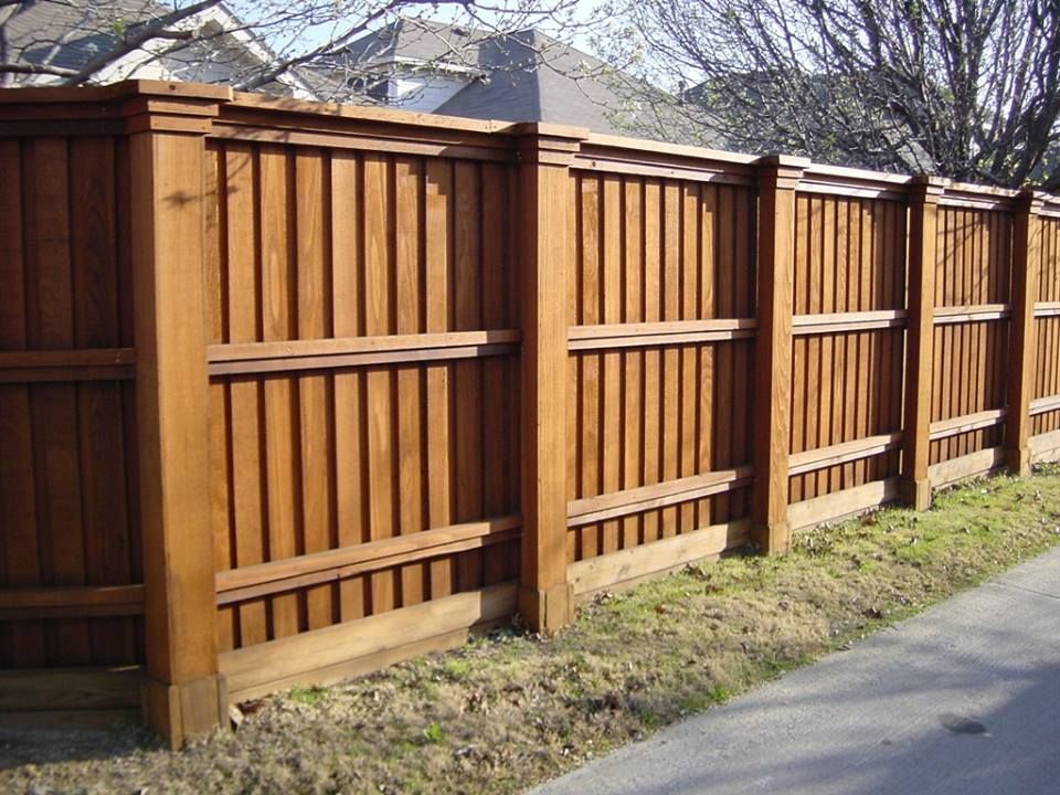 Wooden privacy fence, stained brown, lining a sidewalk next to grass.