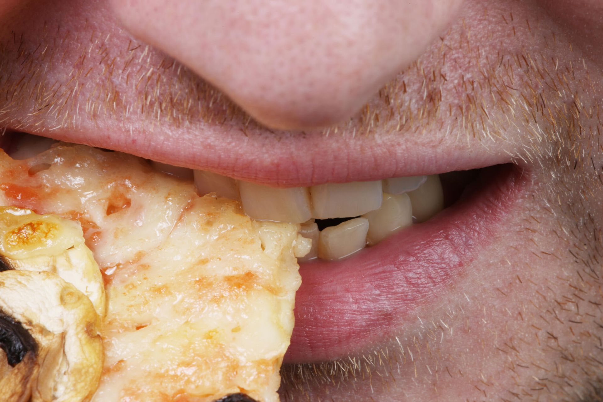 Person taking a bite of a pizza slice, close-up on mouth, cheese visible, skin tones.