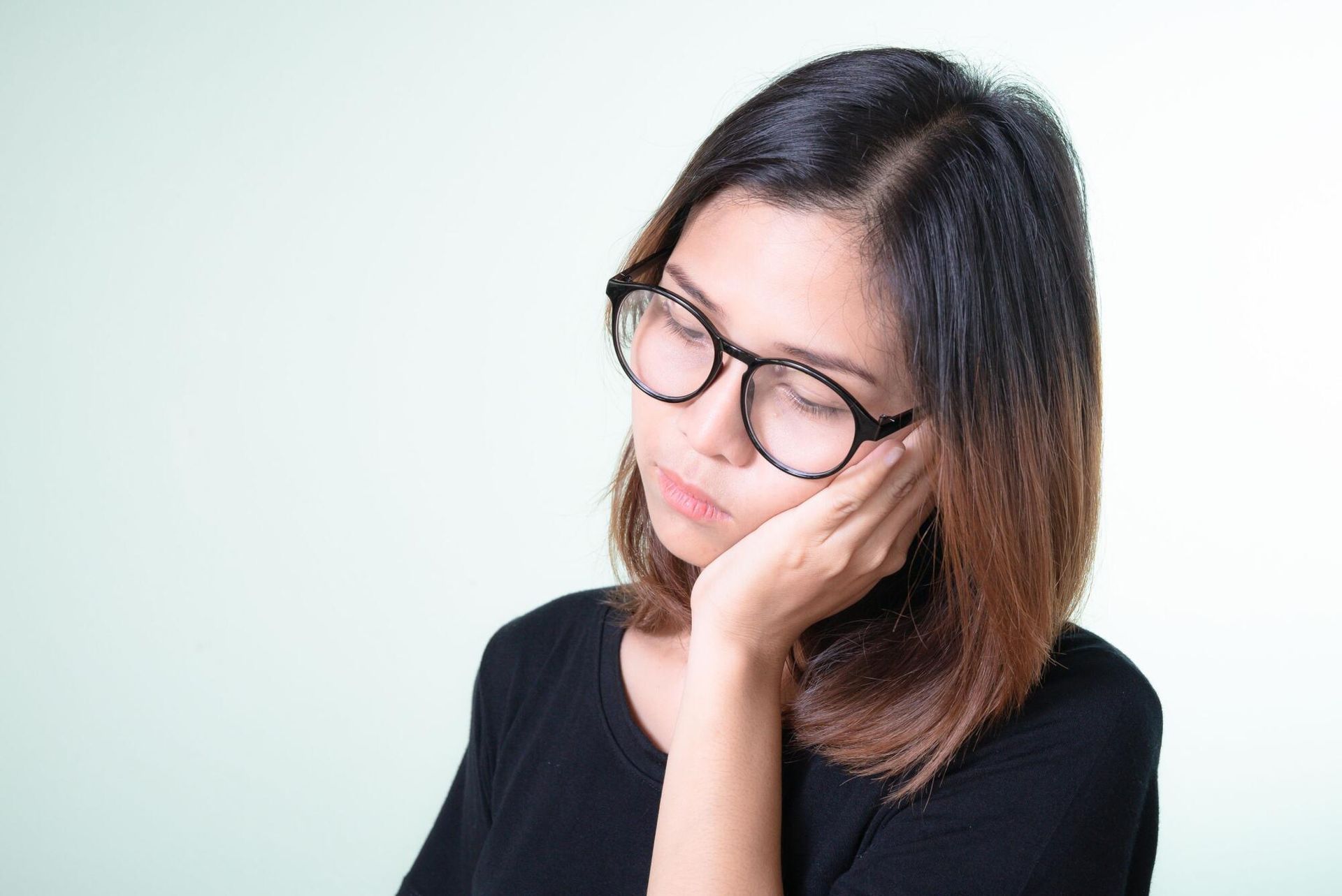 Person with glasses resting their face on their hand against a light background