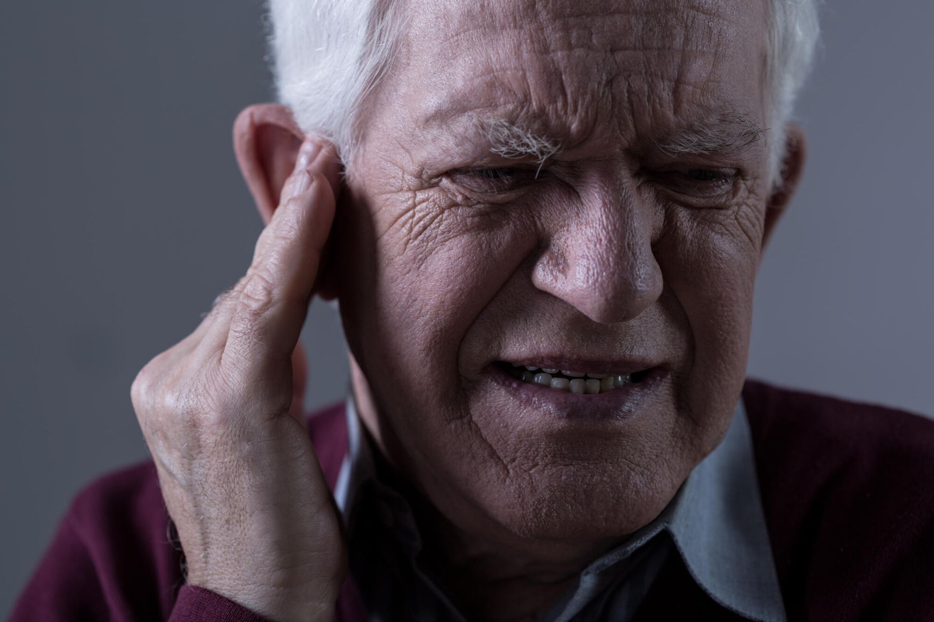 An elderly man is holding his ear because he has a headache.