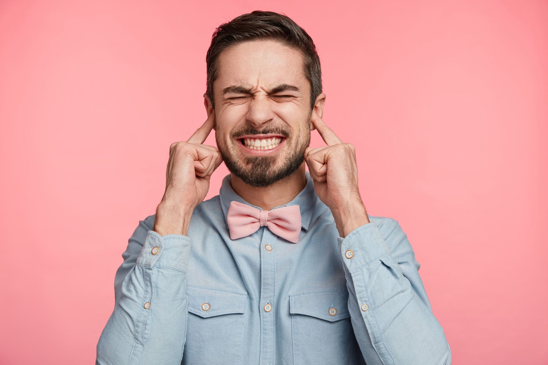 a man wearing a pink bow tie is covering his ears