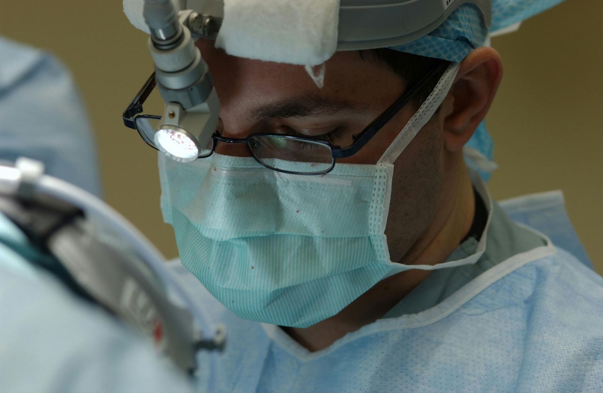 Surgeon wearing a mask and headlamp, focused during an operation.