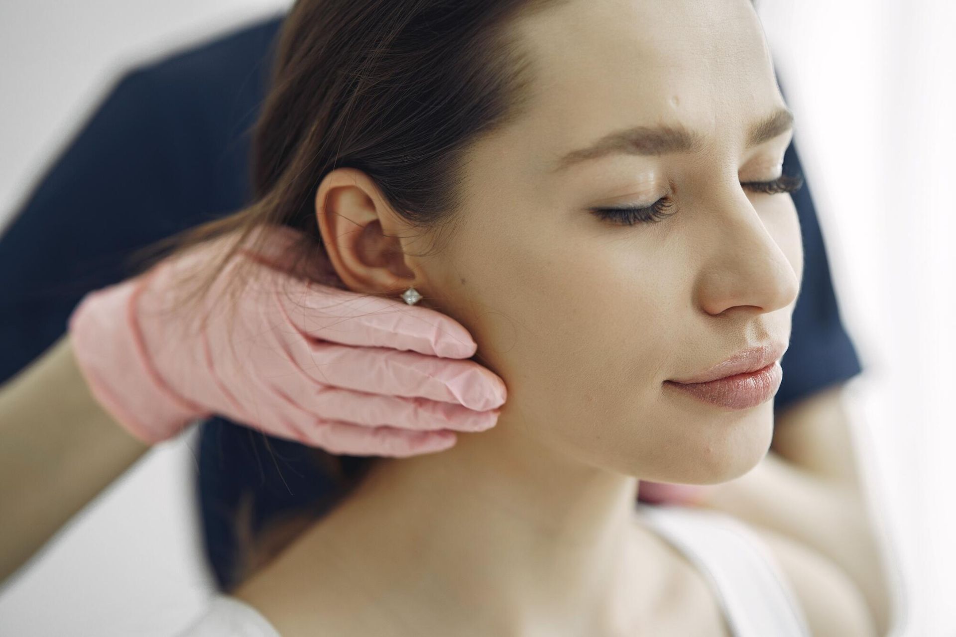 Gloved hand gently touching a woman’s cheek during a facial treatment