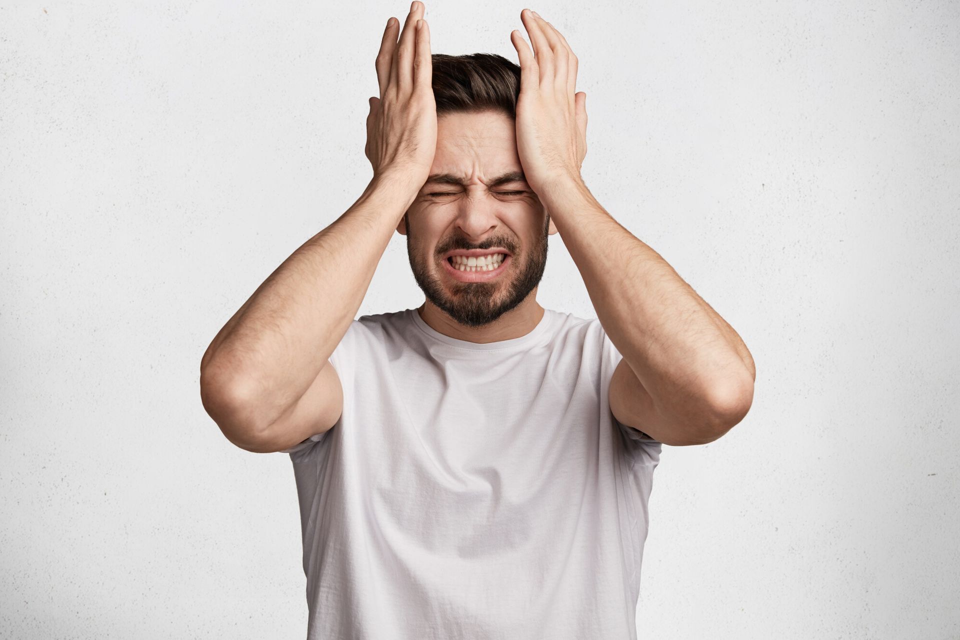 a man in a white shirt holds his head in pain