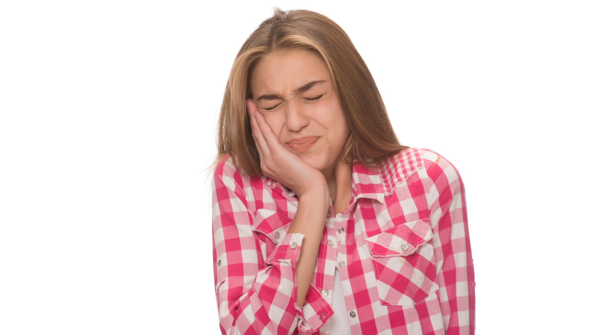 A person wearing a pink plaid shirt holds their hand against their cheek with a pained expression.