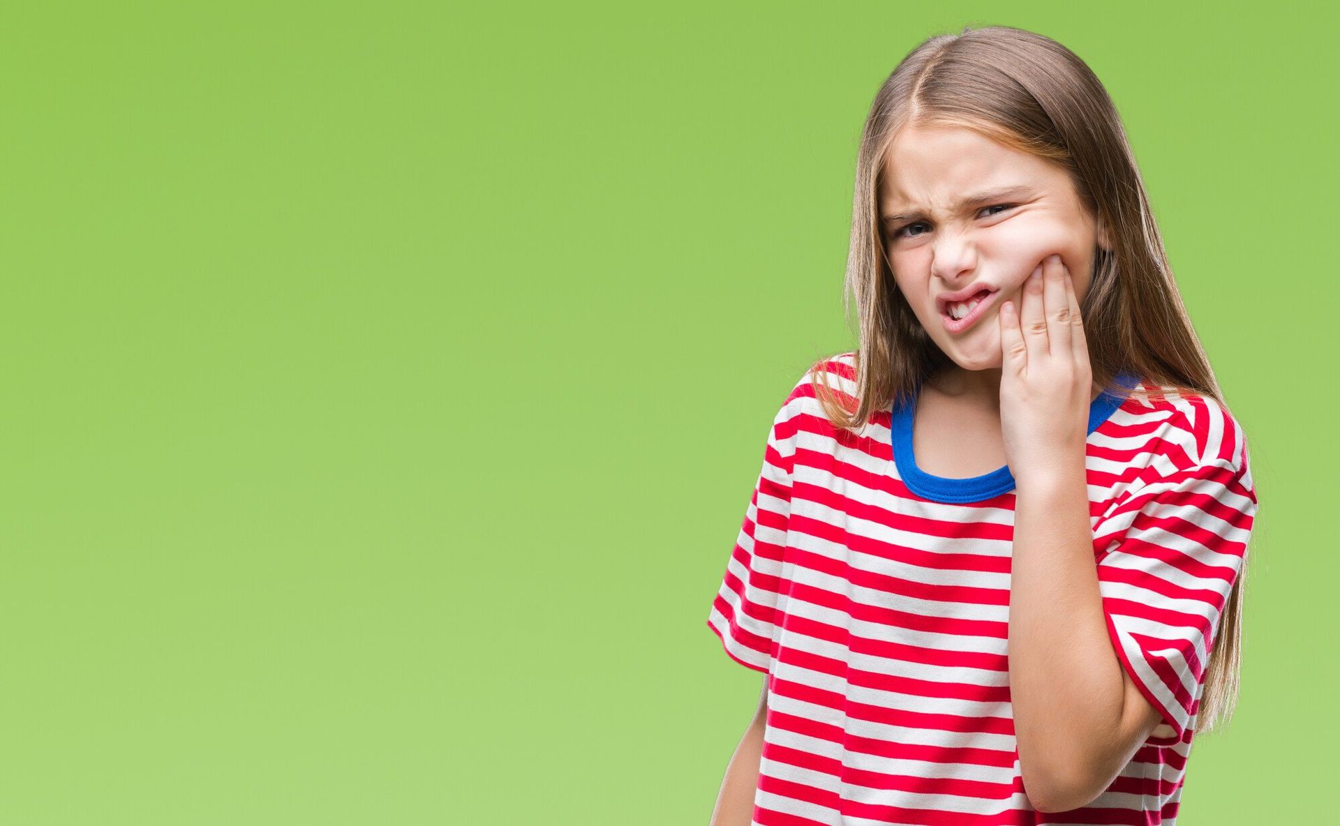 young girl in striped shirt pressing fingers to cheek in pain