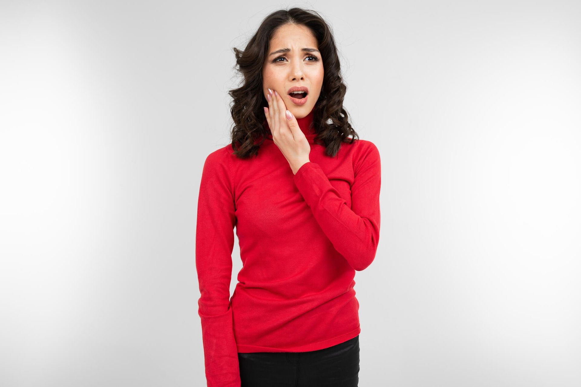 Woman in red turtleneck holds jaw, grimacing with open mouth.