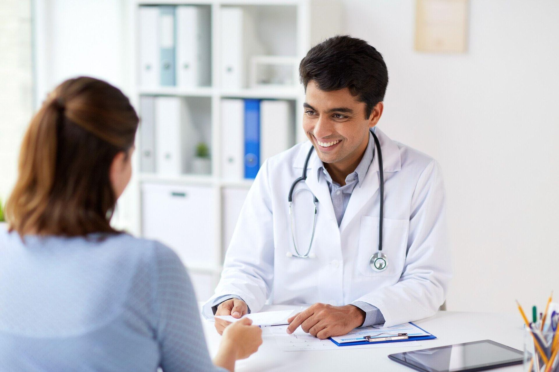 A doctor is sitting at a desk talking to a patient.