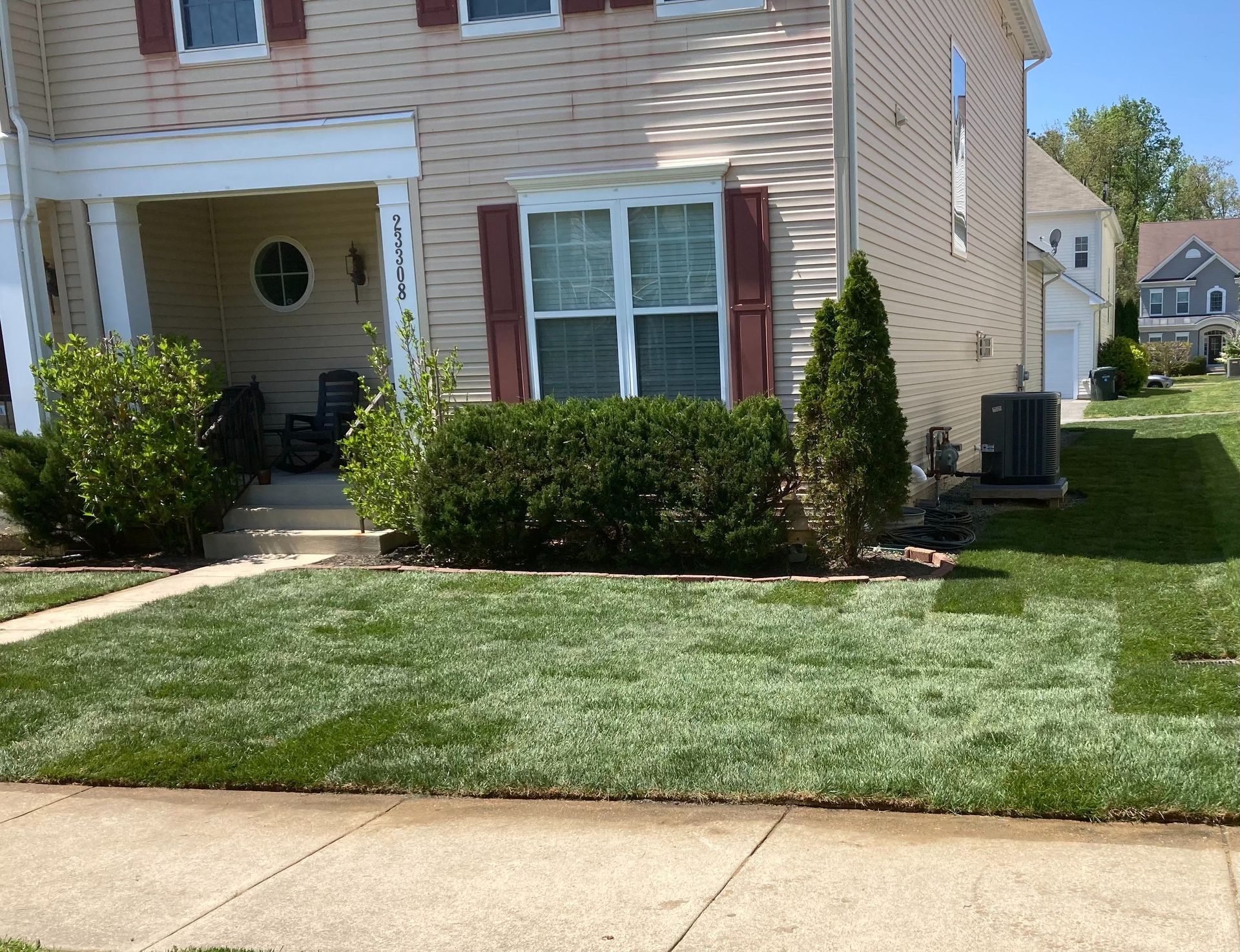 Suburban house with beige siding, trimmed hedges, and a neatly mowed front lawn by the sidewalk
